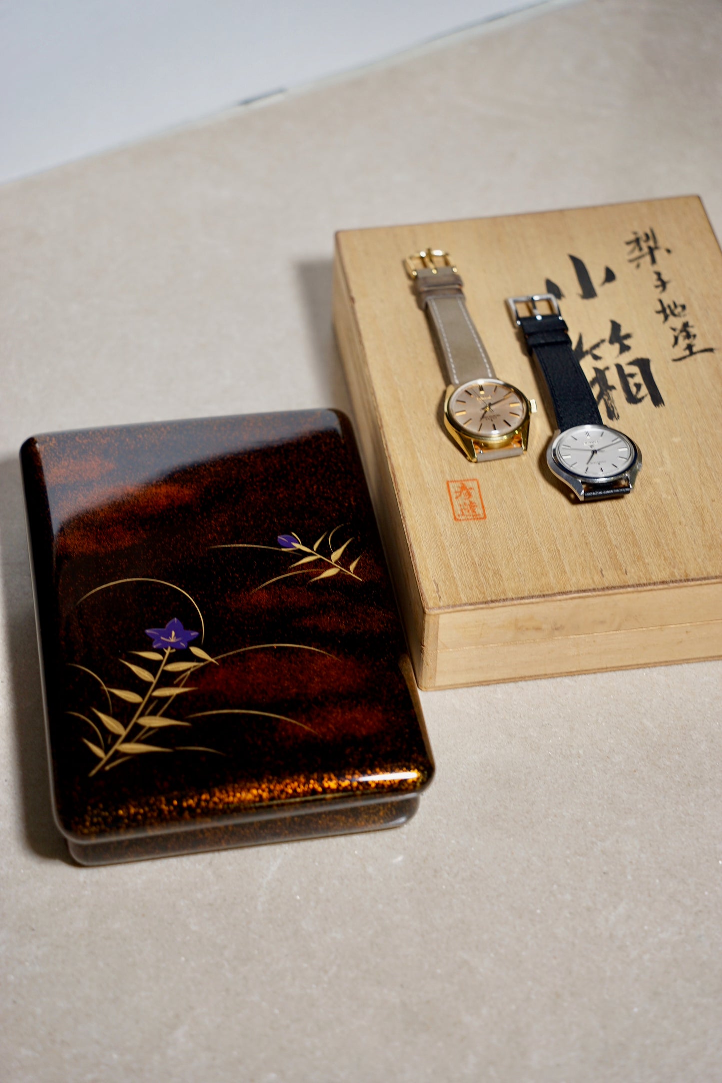 Two watches on a wooden box with decorative lid featuring floral designs.