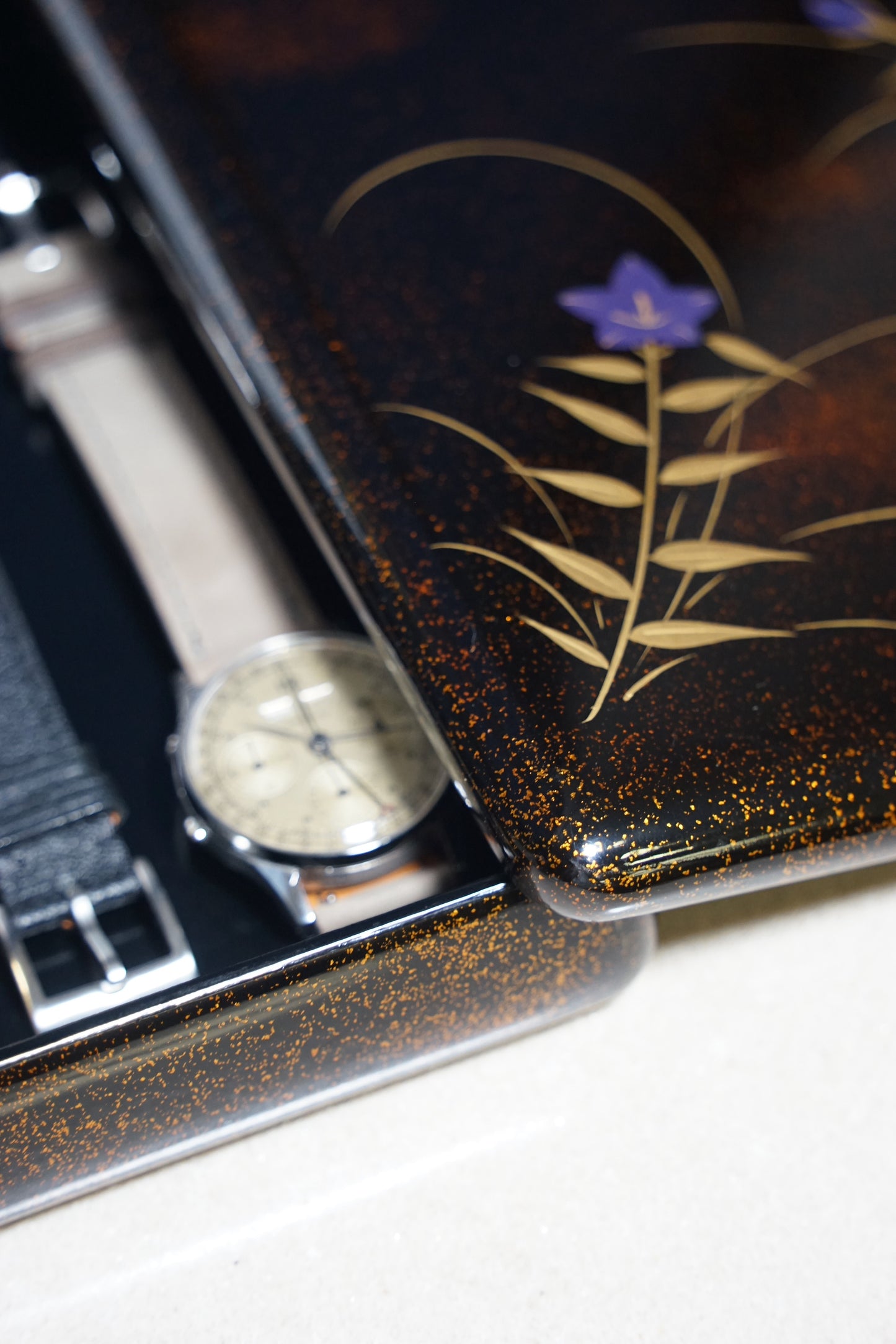 Japanese urushi watch box with floral design and watch on a white surface
