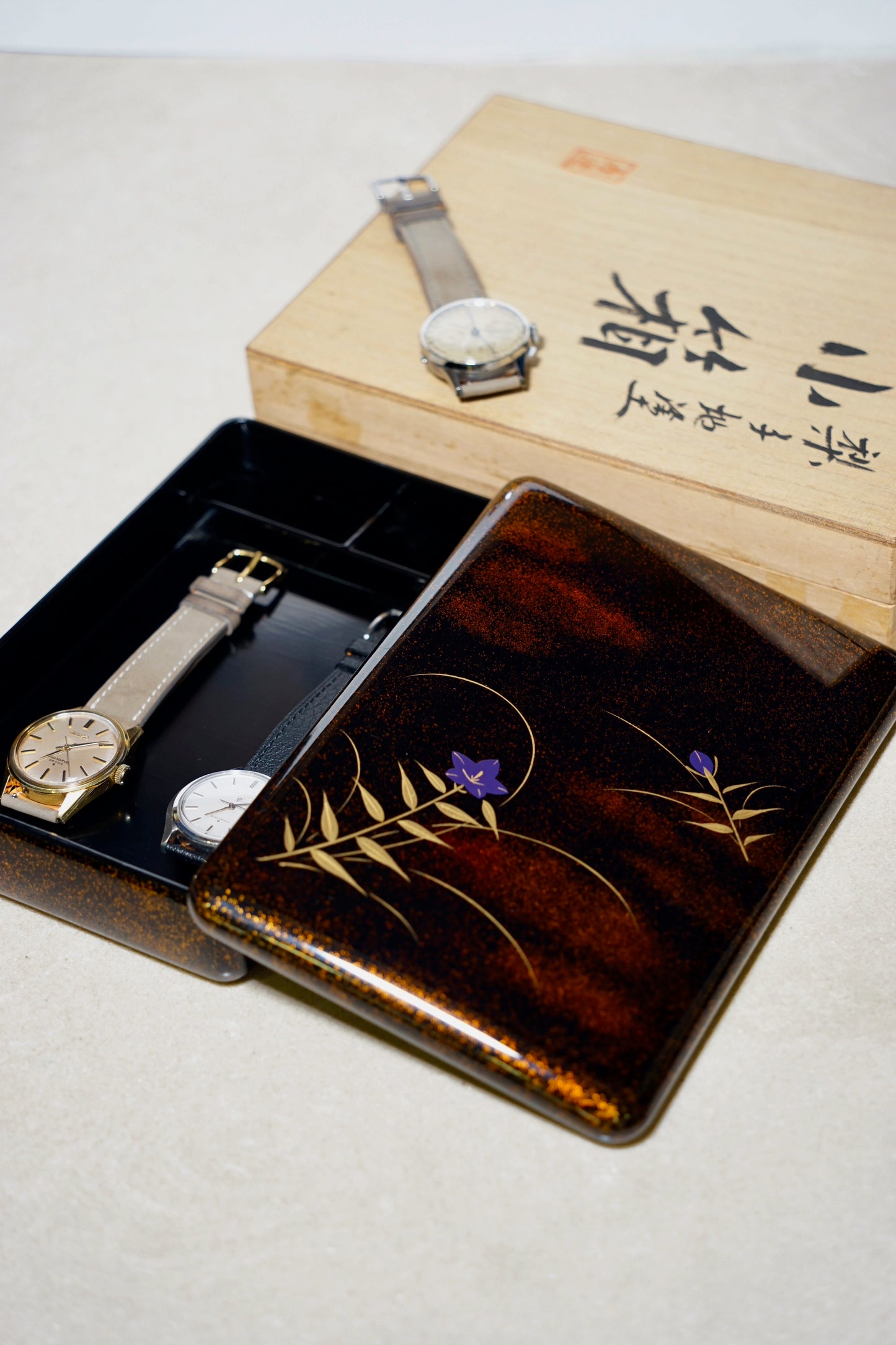 Two watches on a japanese urushi watch decorative wooden box with floral designs.