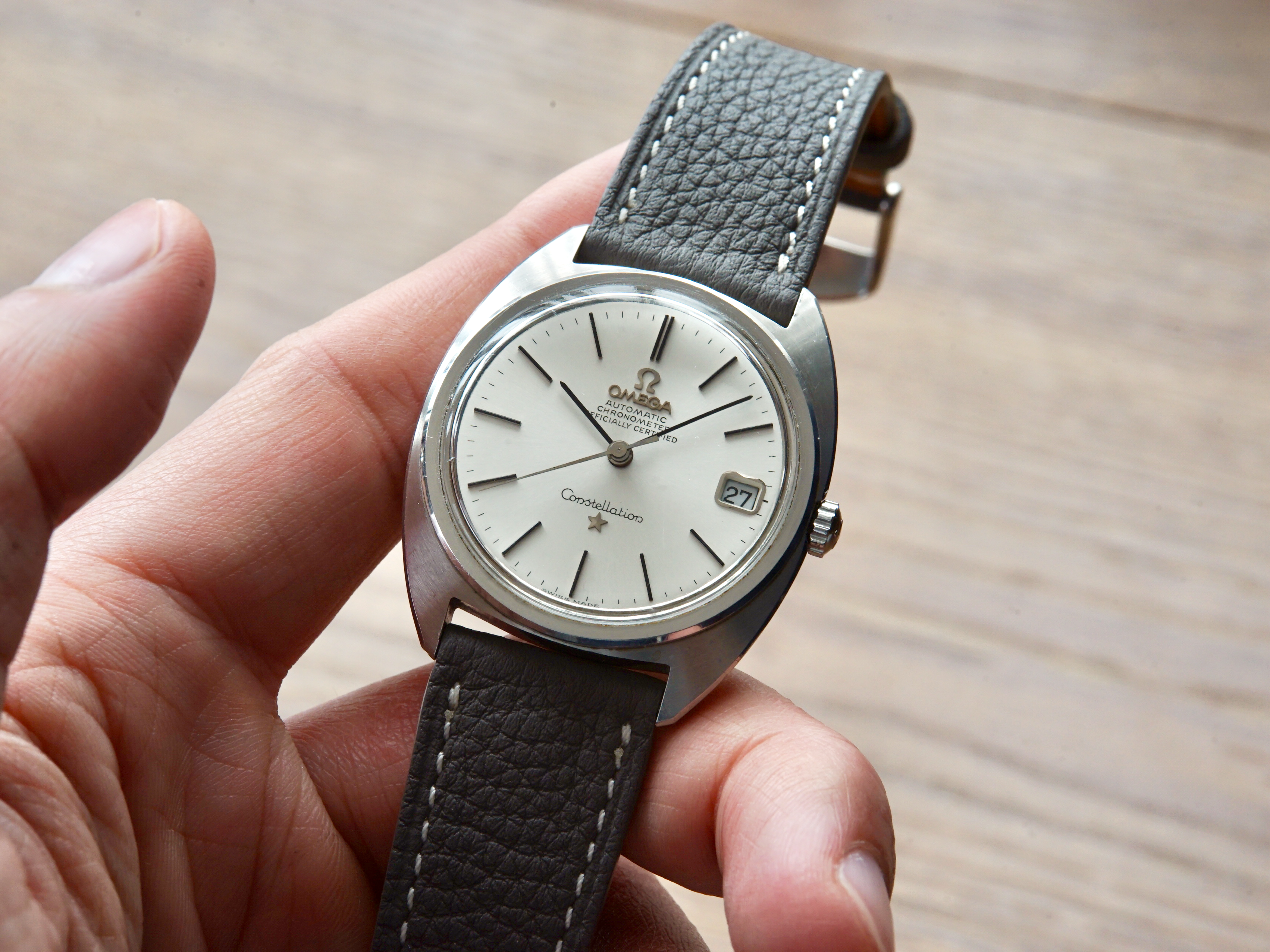 Hand holding a vintage omega constellation watch with a grey togo leather strap