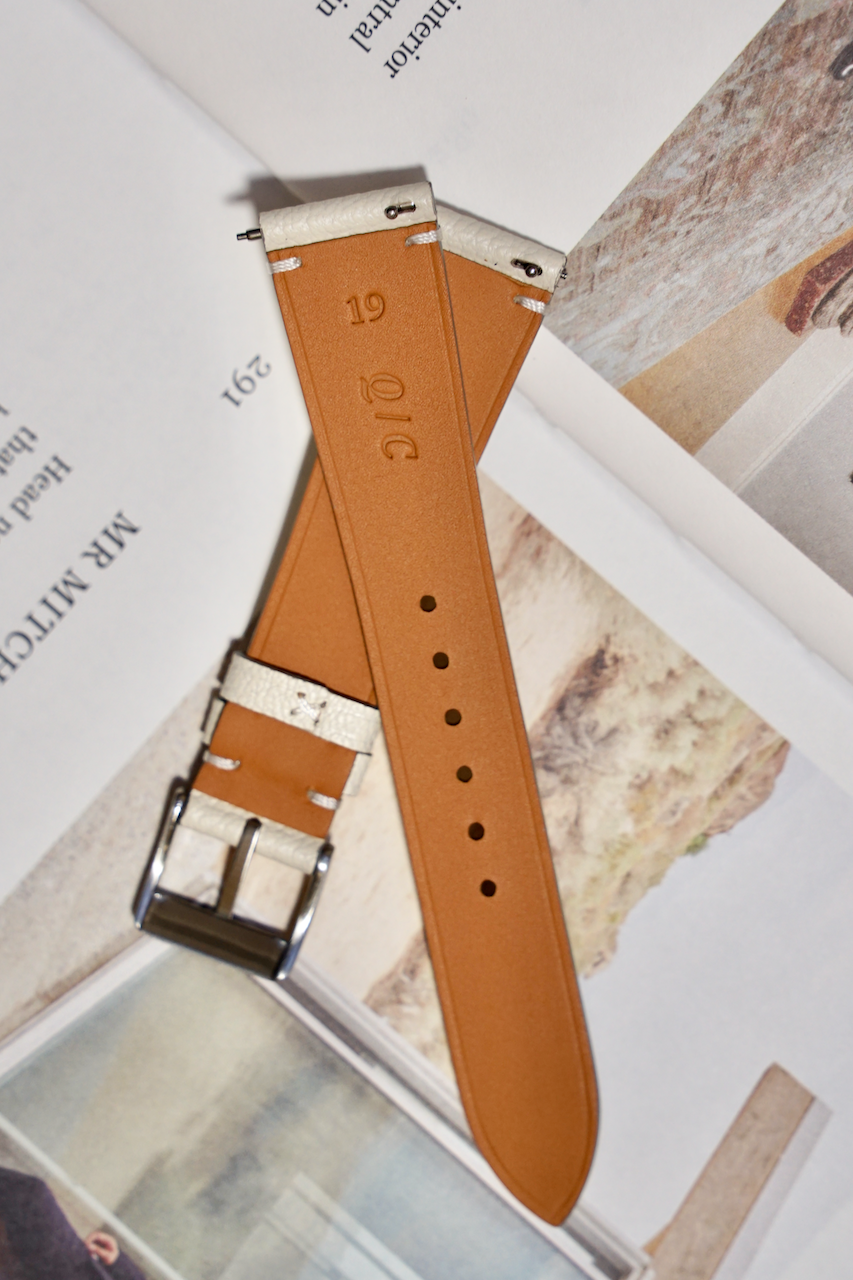 Back of White cream leather watch strap with silver buckle on a textured surface