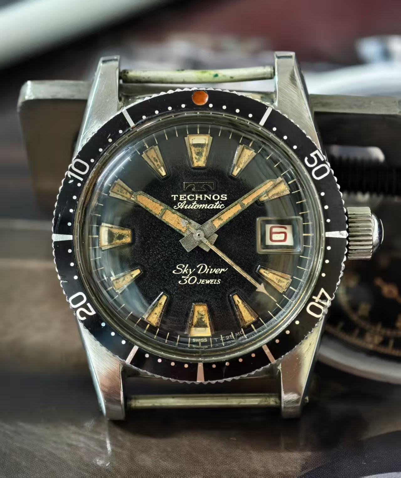 Vintage Technos watch with black dial and silver case on a blurred background