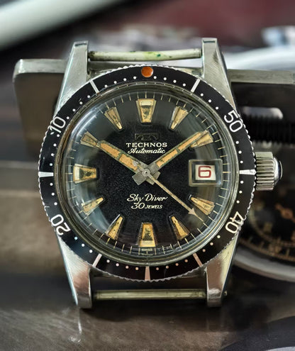 Vintage Technos watch with black dial and silver case on a blurred background