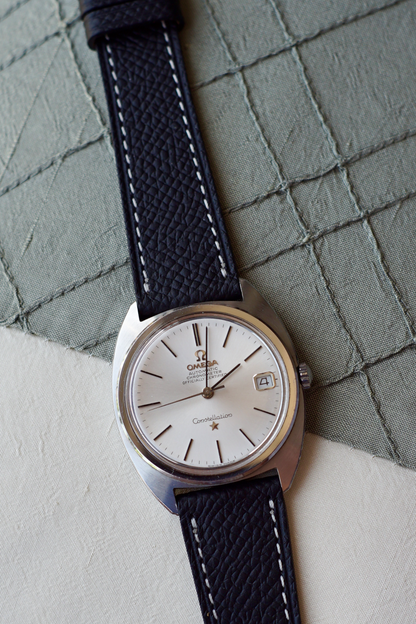 Vintage Omega watch with black leather strap on a textured surface