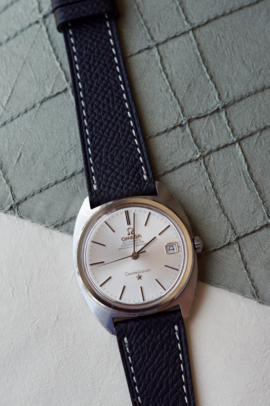 Vintage Omega watch with black leather strap on a textured surface